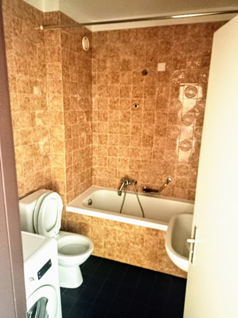 Bathroom with beige tile walls, a bathtub, and a toilet
