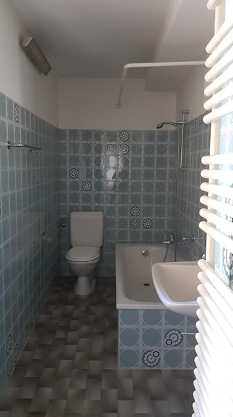 Tiled bathroom with a toilet, bathtub, and shower. The walls are covered in a patterned tile design.