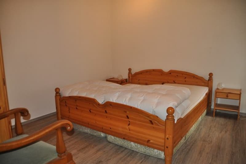 Wooden bed with white bedspread, two nightstands, wooden chair, wooden floors