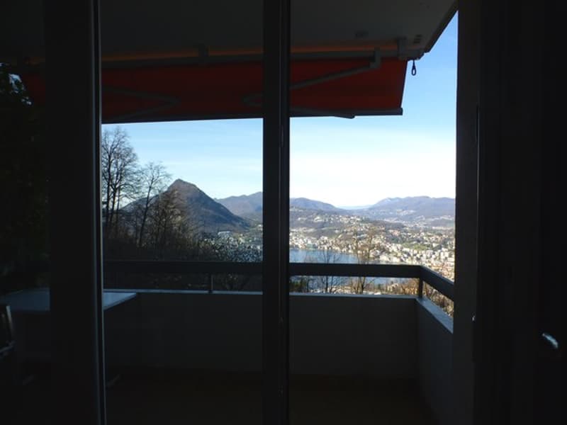 Terrace with mountain view, balcony, glass doors, trees, lake, and town below