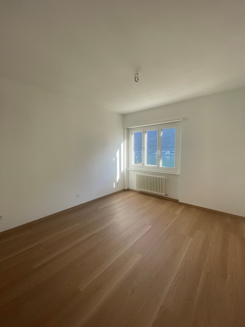 empty room, white walls, wooden floor, a window with a view of the water