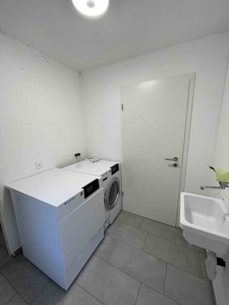 Laundry room with white tiled floor, sink, washing machine, and dishwasher.