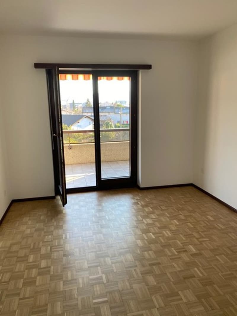Empty room with hardwood flooring, large window with sliding glass door leading to a balcony or terrace, and white walls.
