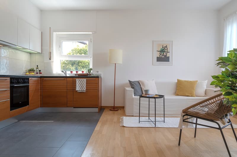 modern kitchen with wooden cabinets, black oven, white tiled backsplash, white couch, side table, floor lamp, wicker chair, plant