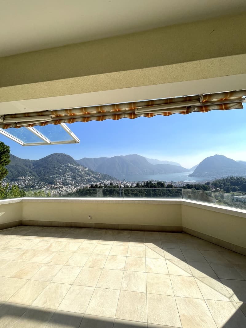 Empty balcony with tiled floor, retractable awning, and panoramic view of mountains and a lake.