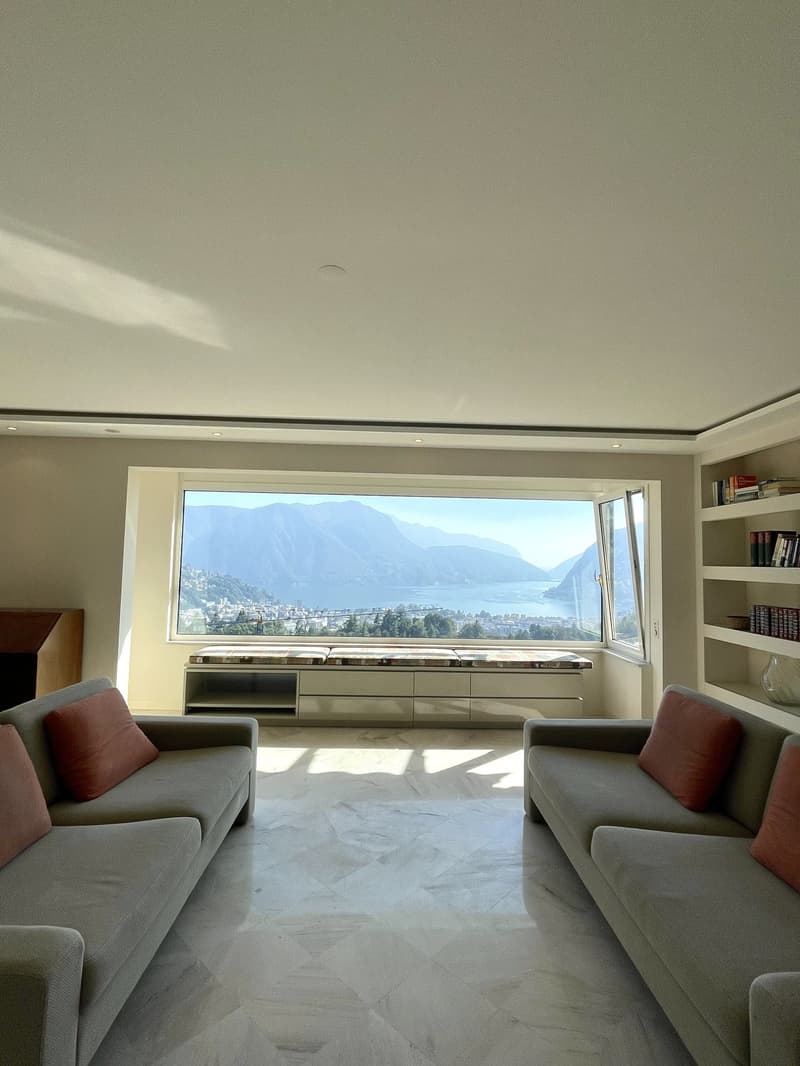 Spacious living room with large windows, couches, and a view of the mountains and lake.
