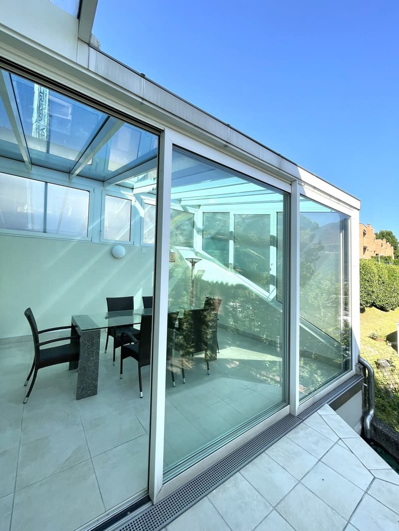 Modern balcony with glass walls, tiled floor, and a dining set with a glass table and chairs.