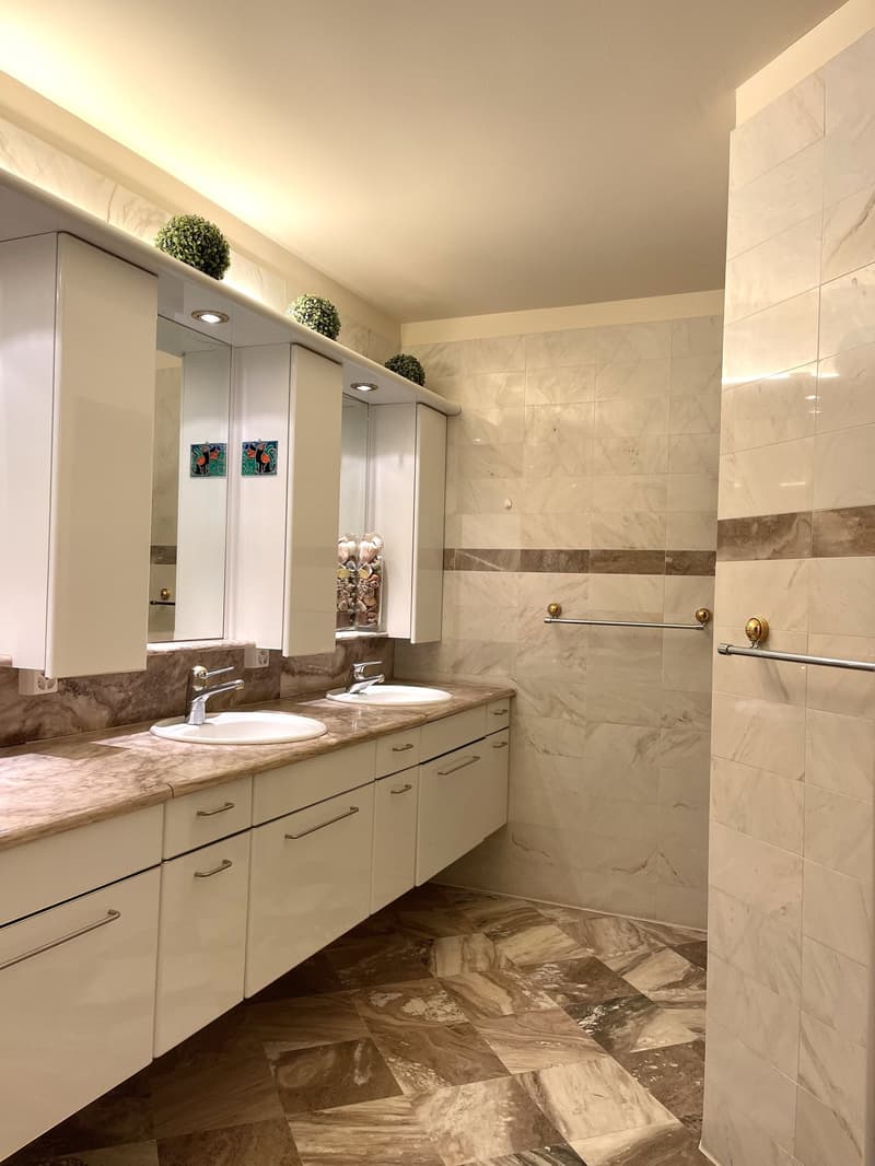 Modern bathroom with marble flooring, white cabinets, double sinks, and a large mirror.