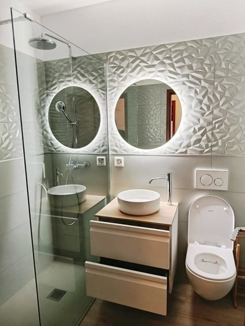 contemporary bathroom with walk-in shower, round mirrors, wooden vanity, floating toilet, white tiles, glass door
