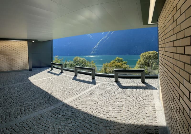 Outdoor parking area with a view of the lake and mountains, metal railings, brick walls, stone pavement.