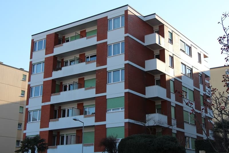 Modern apartment building, red brick, white trim, balconies, streetlight