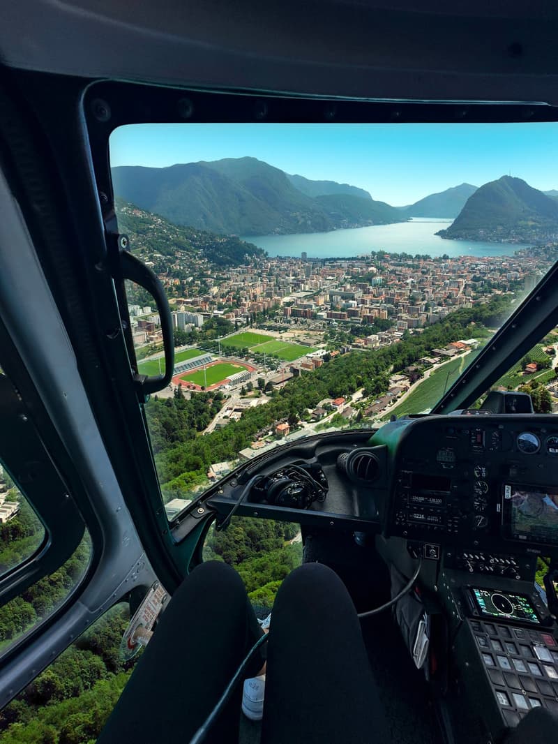 Aerial view of a city with mountains, a lake, and a green field