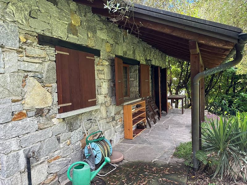 stone building, brown shutters, awning, wooden desk, shelf, chairs, garden hose, watering can