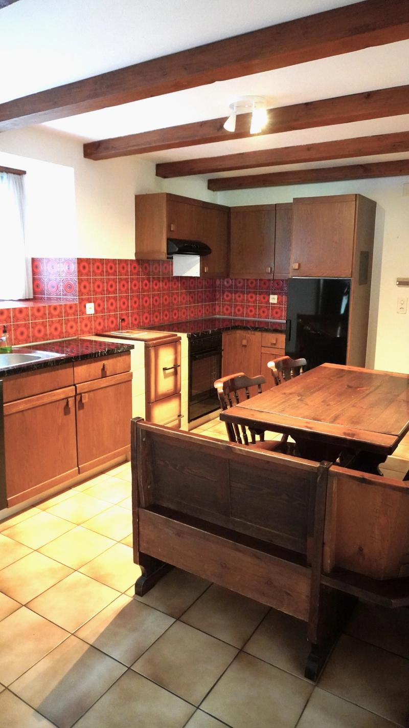 Wooden kitchen furniture, red tiled wall, wooden dining table, chairs, built-in bench, black fridge, tiled floor