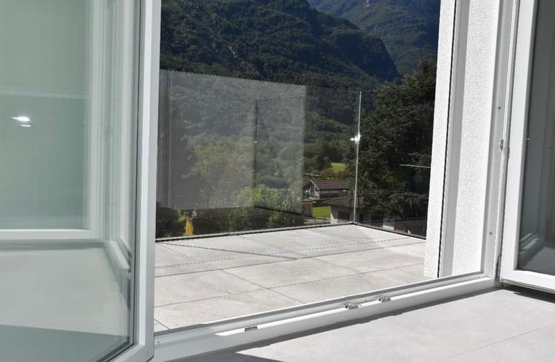 Large windows with a view of the mountainous landscape outside, concrete floor, white walls