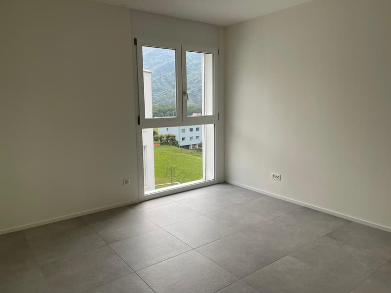 Spacious bedroom with large windows, providing a view of the surrounding greenery. The room has a tiled floor and neutral-colored walls, creating a clean and modern look.