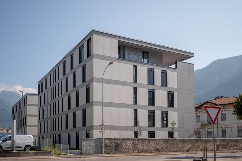 modern grey concrete building, 4 floors, windows, balconies, surrounded by mountains