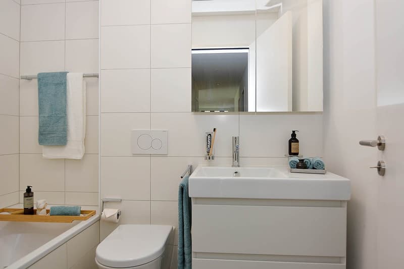 White tiles, toilet, bathtub, sink, mirror, towels, toiletries, toilet paper
