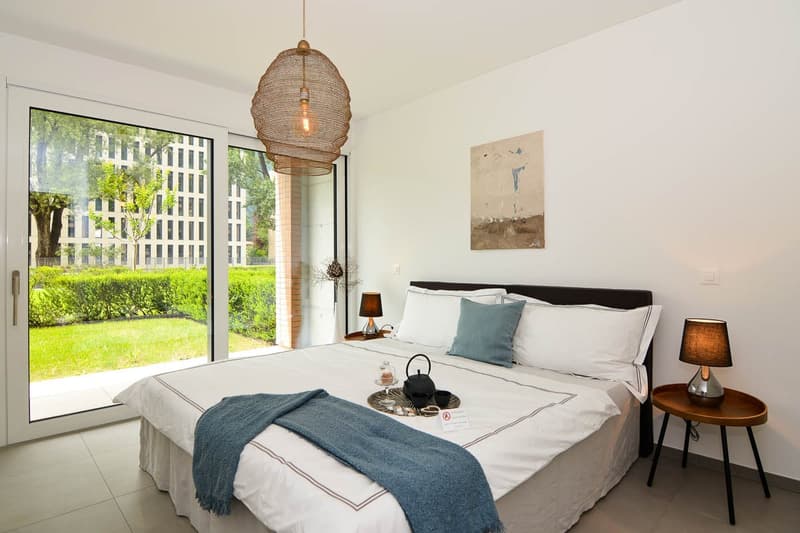 A bed, two nightstands with lamps, a framed artwork, a sliding glass door, a lamp hanging from the ceiling, a teapot and a tray on the bed