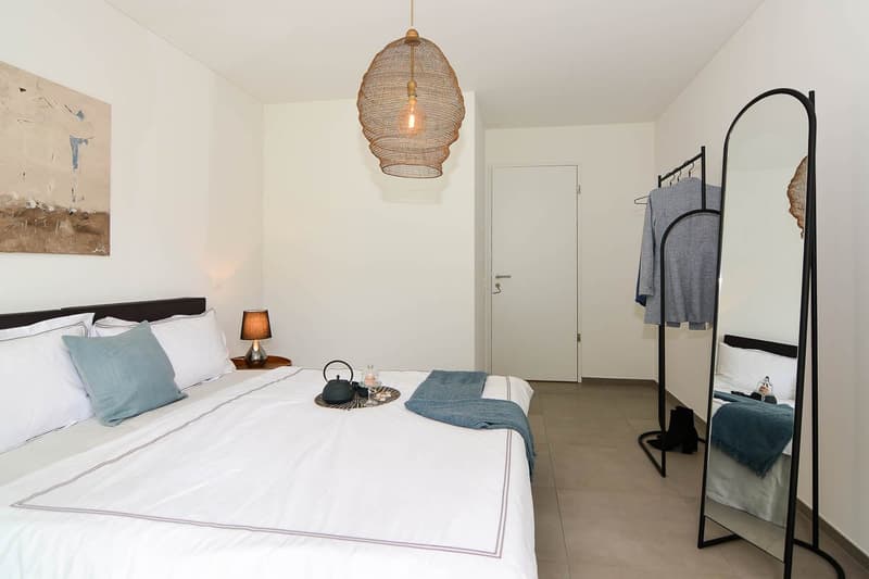 white walls, beige tiles, bed, lamp, decorative items on tray, mirror, wardrobe, door
