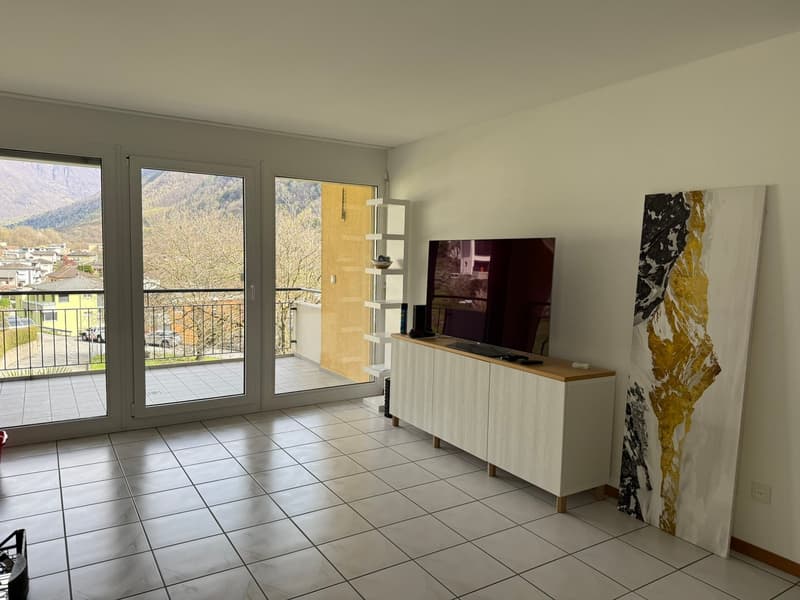 Spacious living room with large windows providing a scenic view, tiled flooring, a TV stand with a TV, and a decorative abstract art piece on the wall.