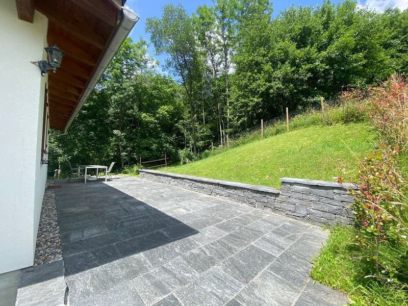 Stone patio, surrounded by grassy hillside, fenced area, outside table and chairs