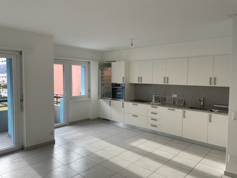Spacious open-plan kitchen and living area, white cabinets, gray countertops, tiled flooring, large windows, and access to a balcony or terrace.