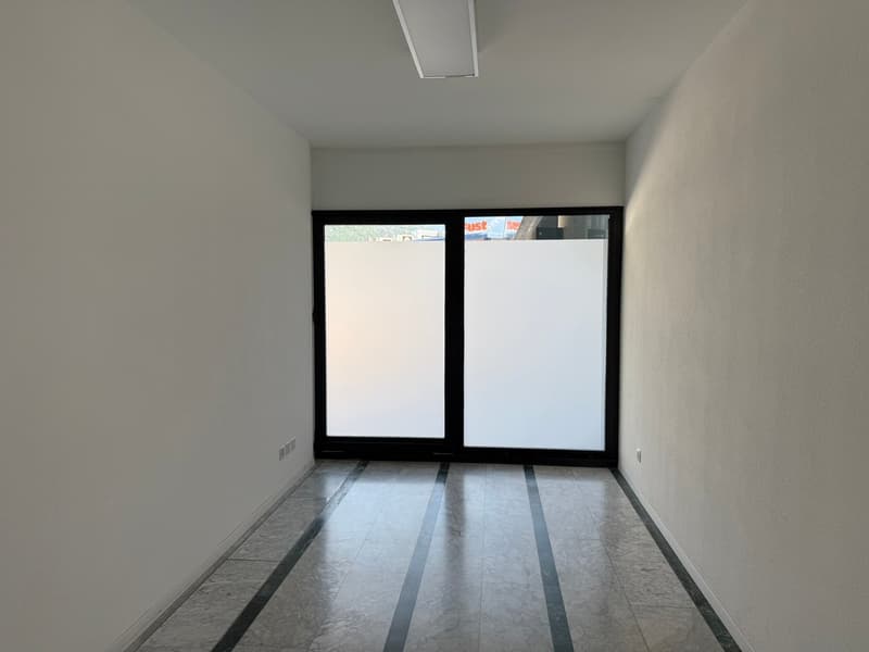 Empty room with white walls, large windows, and a tiled floor.