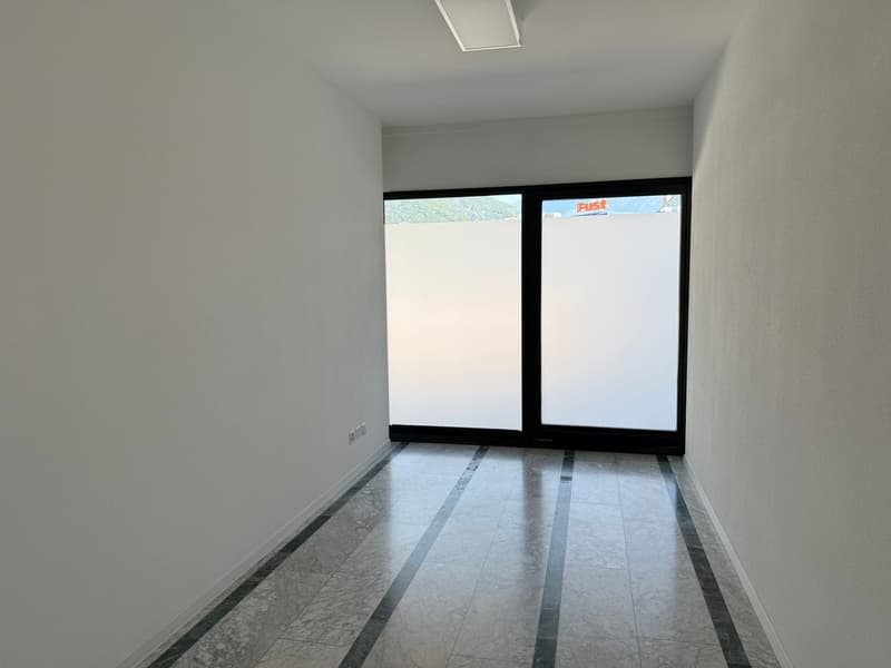 Empty room with white walls, gray tile flooring, and large windows providing natural light.