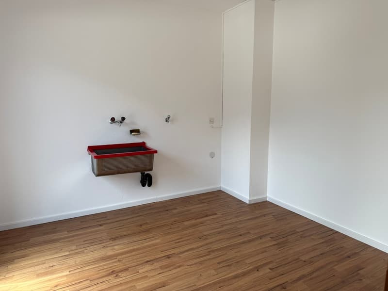 Empty room with white walls, hardwood floor, and a red storage container on the wall.