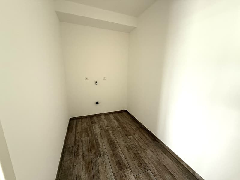 Empty room with white walls and dark wood-look tile flooring.