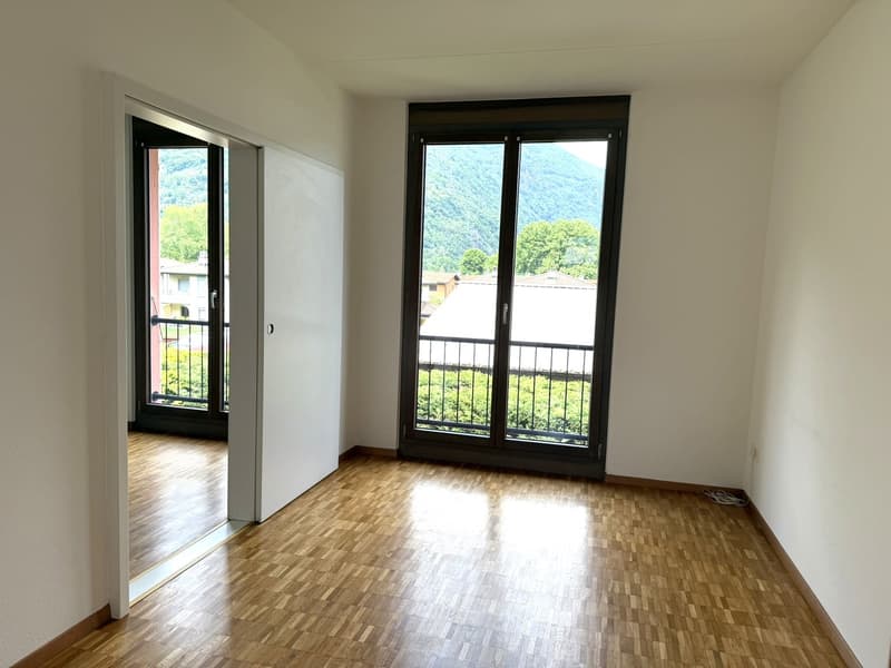 Spacious bedroom with hardwood flooring, large windows providing a scenic view of the surrounding mountains and greenery, and a sliding glass door leading to a balcony or terrace.