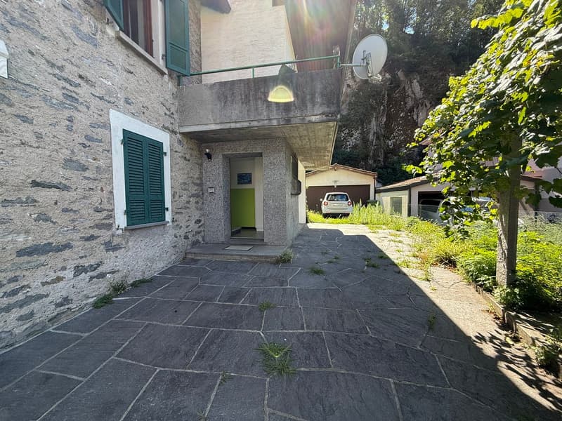 2-story stone house with green shutters, stone patio, garage, and surrounding greenery