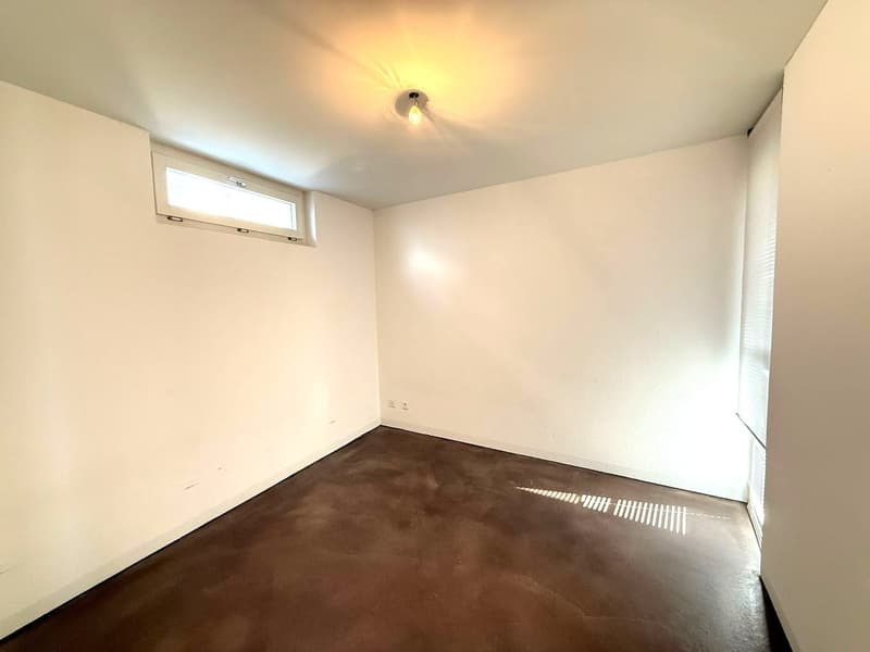 Empty room, white walls, brown wooden floor, single ceiling light, small window.