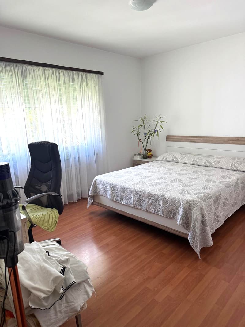 double bed, white sheets, bed headboard, nightstand, flowers, black chair, white curtains, hard wood floor