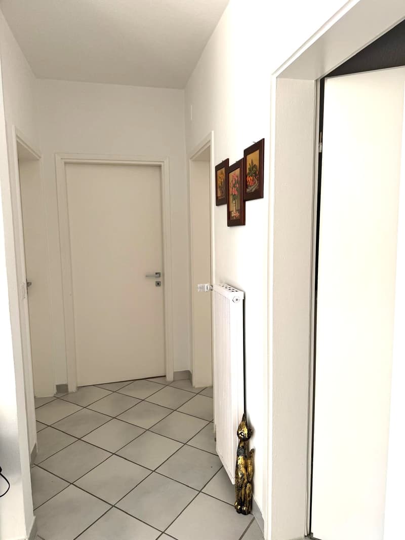 tiled floor, white walls, closed doors, pictures on wall, white radiator, black wire