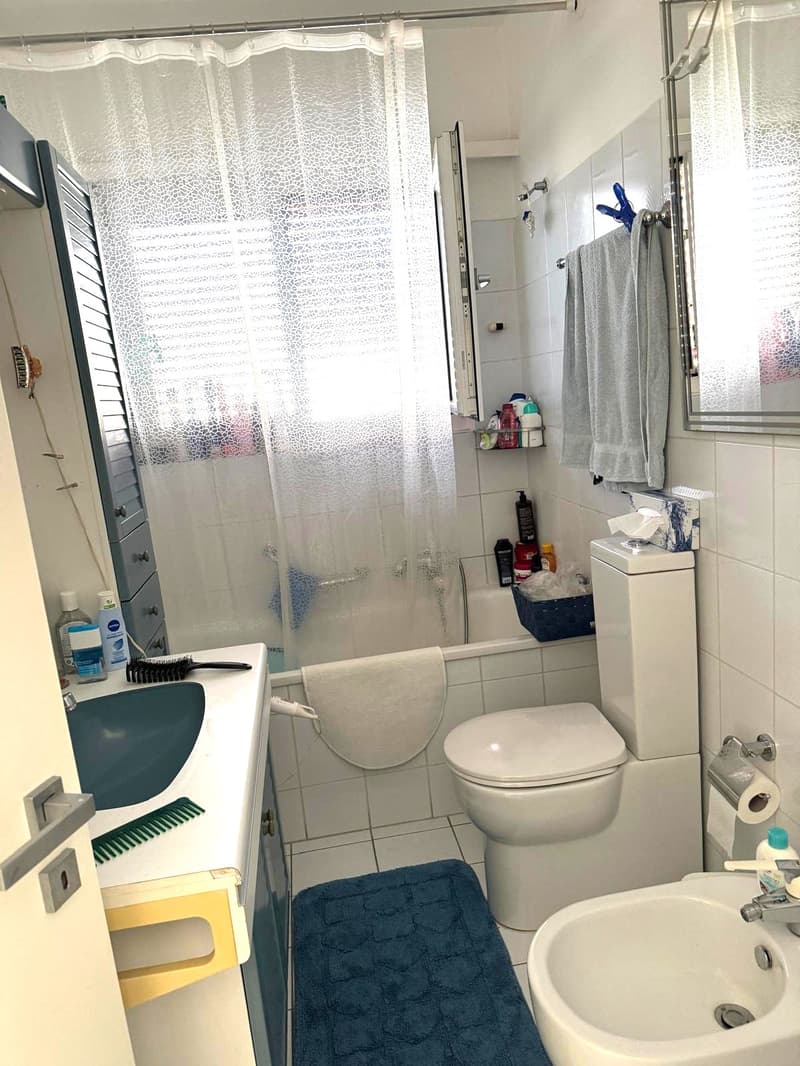 a white bathtub, white sink, white toilet, shower curtain, toiletries, towels, blue rug