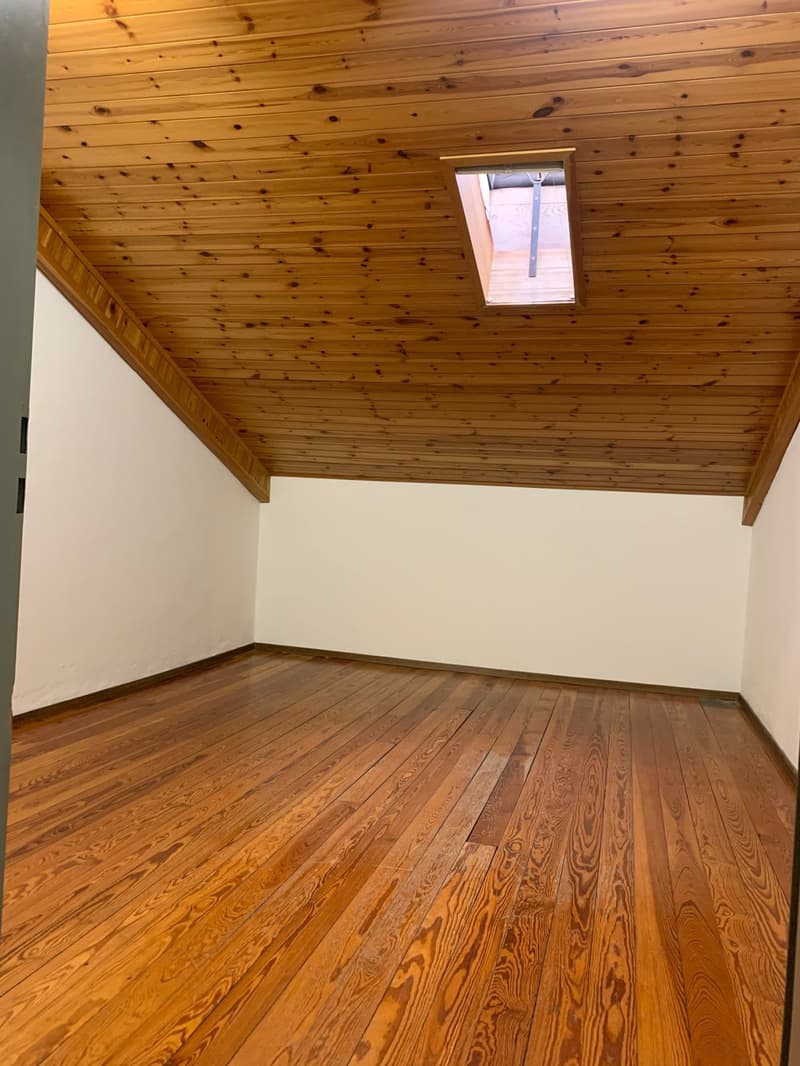 Empty room with wooden floors, white walls, wooden ceiling, and a small skylight window