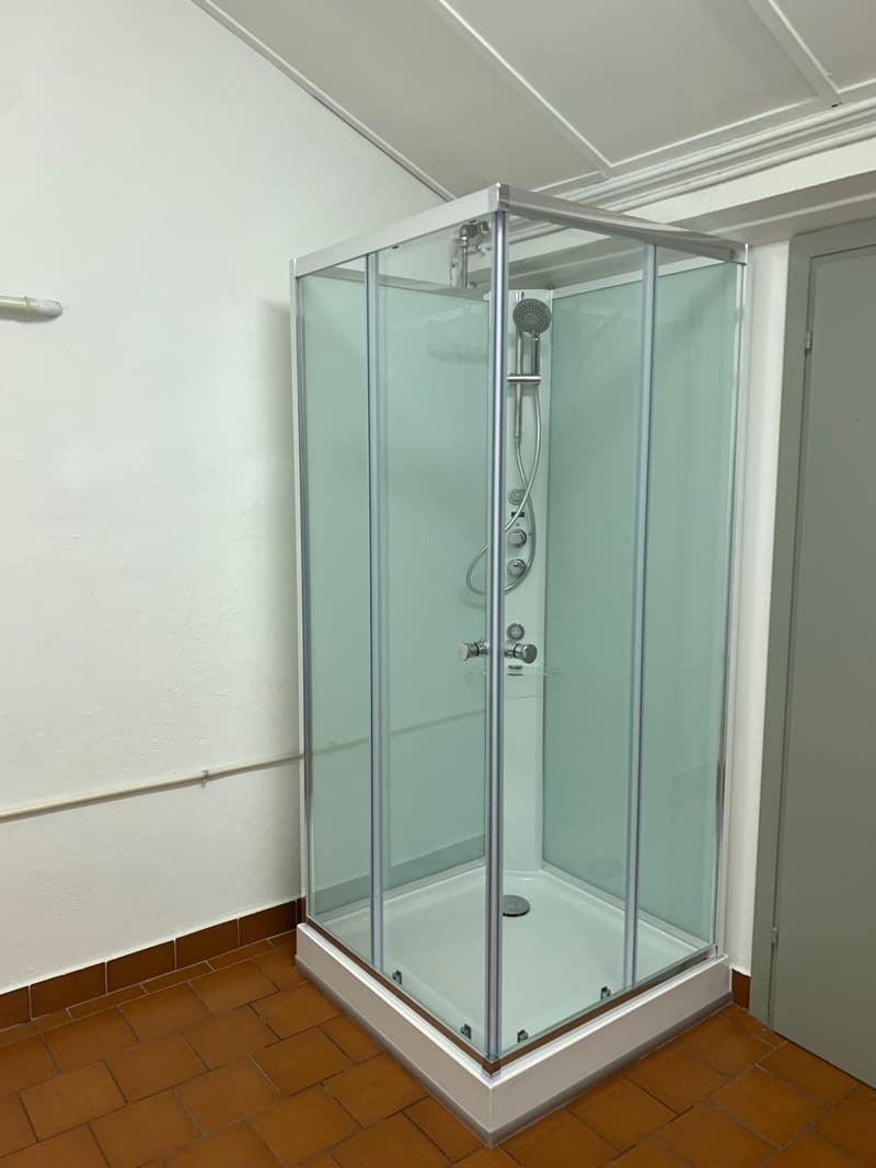 Shower stall, glass walls, silver trim, water dispenser, metal handles, tiled floor