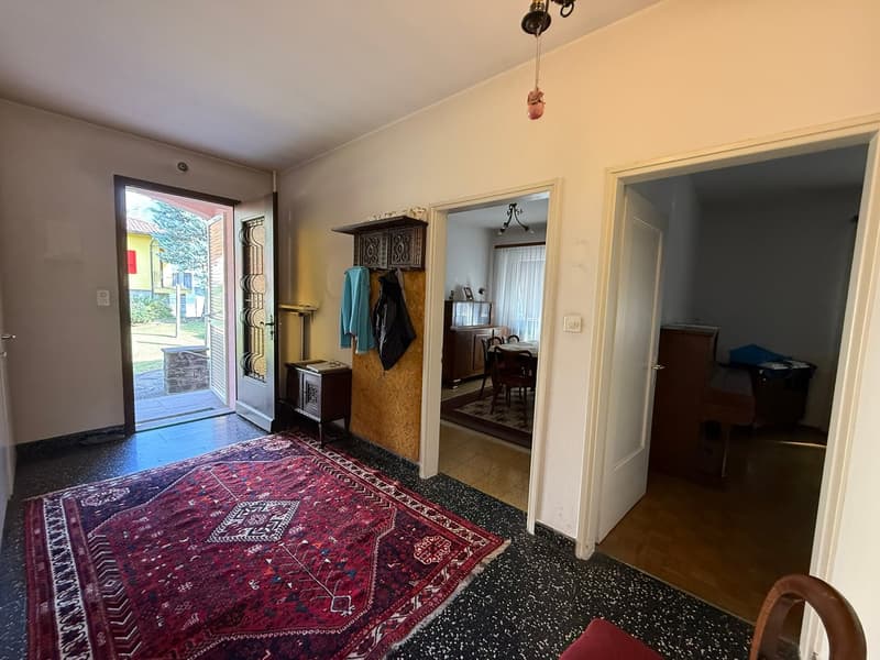 room with floor covered by red carpet, an open door, a wooden cabinet, hanging lamp and a coat stand