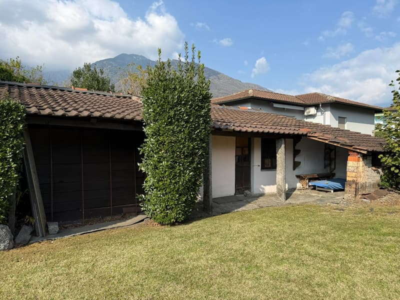 A house with brown roof, white walls, a garage with a large brown door, a front yard with green grass, and a mountain view in the background.