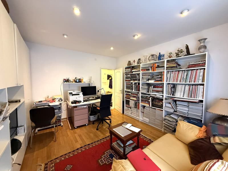 A room with a desk, chair, printer, computer, lamp, couch, coffee table, rug, bookshelves, and various decorative items.