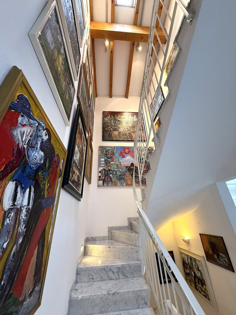 marble staircase, white handrail, white walls, multiple paintings on the wall