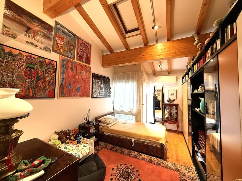 Bedroom with bed, nightstand, lamp, rug, wooden beams, paintings, cabinet, mirror, books, toys