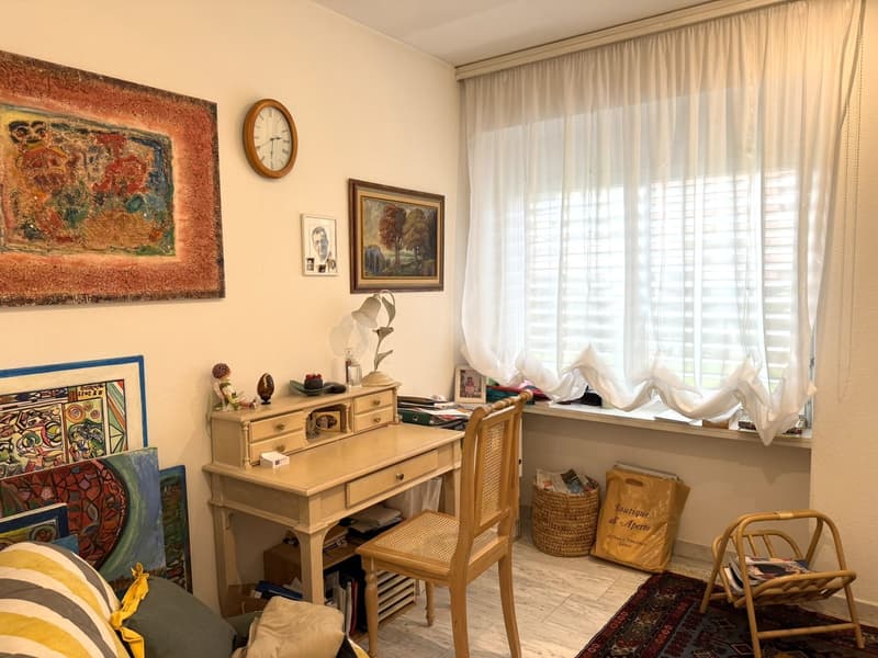 desk, chair, paintings, clock, window with curtains, rug, pillows, basket, bag