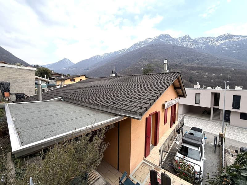 Single-family house with a tiled roof, red doors, and a garage with a car parked in front, located in a mountainous area with a scenic view.