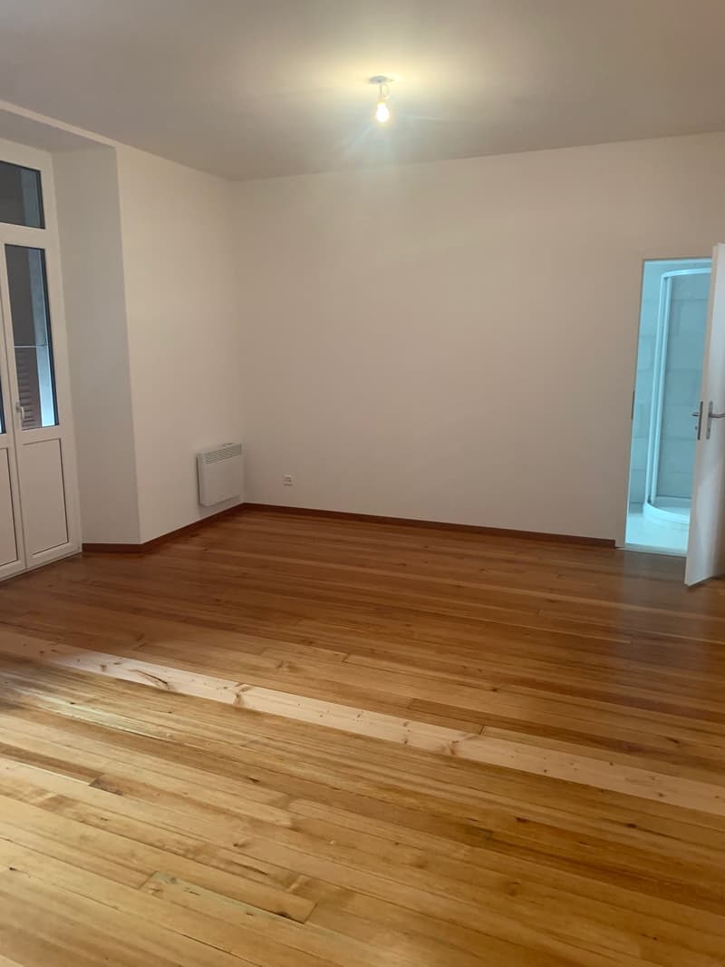 empty room, wooden floor, white walls, ceiling light, two doors, one leading to a bathroom