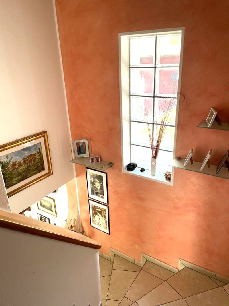 staircase with tiled steps, peach-colored walls, picture frames on the wall, window with a vase