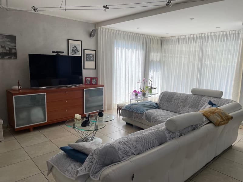 modern living room with white leather couches, glass coffee table, flat screen TV, wooden entertainment center, white curtains