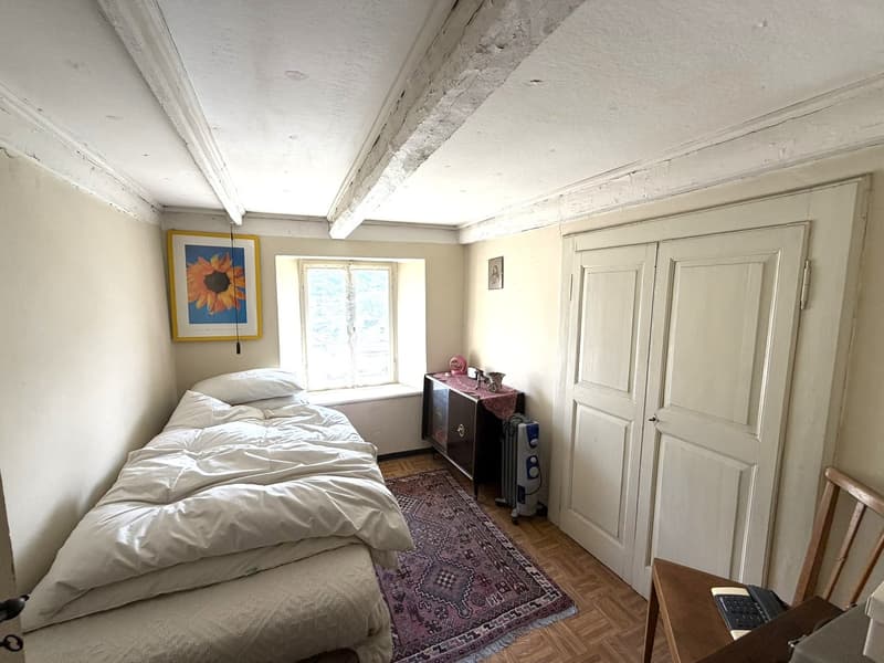 small bedroom with bed, rug, window, wooden floor, wooden chair, desk, radiator, cabinet, picture frame
